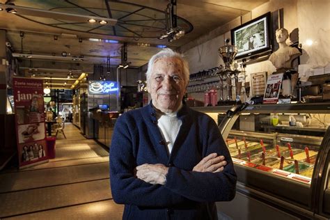 Foto van Elio Talamini, de 90-jarige patriarch van de Talamini ijssalon in Deventer, lachend achter de toonbank.