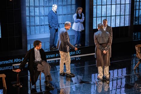 Peter de Baan geeft aanwijzingen aan een groep acteurs op een podium.