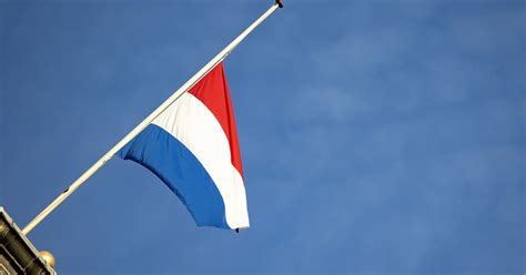 Illustratie van een Nederlandse vlag die correct halfstok hangt aan een vlaggenmast.